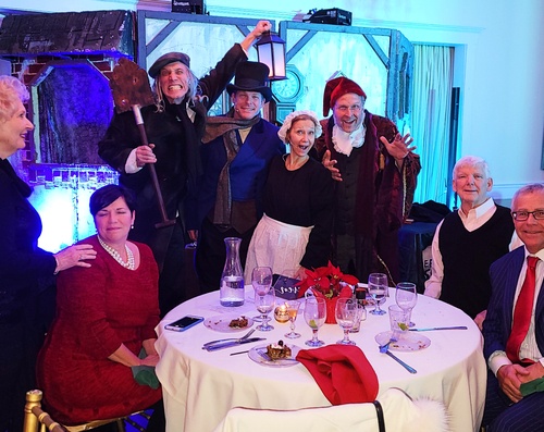 Diners enjoy a holiday feast while watching 'A Christmas Carol' performed live on stage